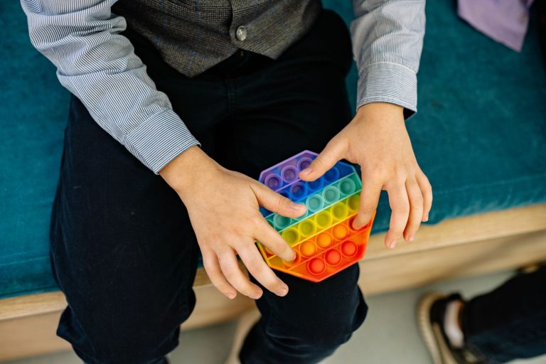 Mains d'un enfant manipulant un pop it arc-en-ciel, un fidget sensoriel, posé sur ses genoux